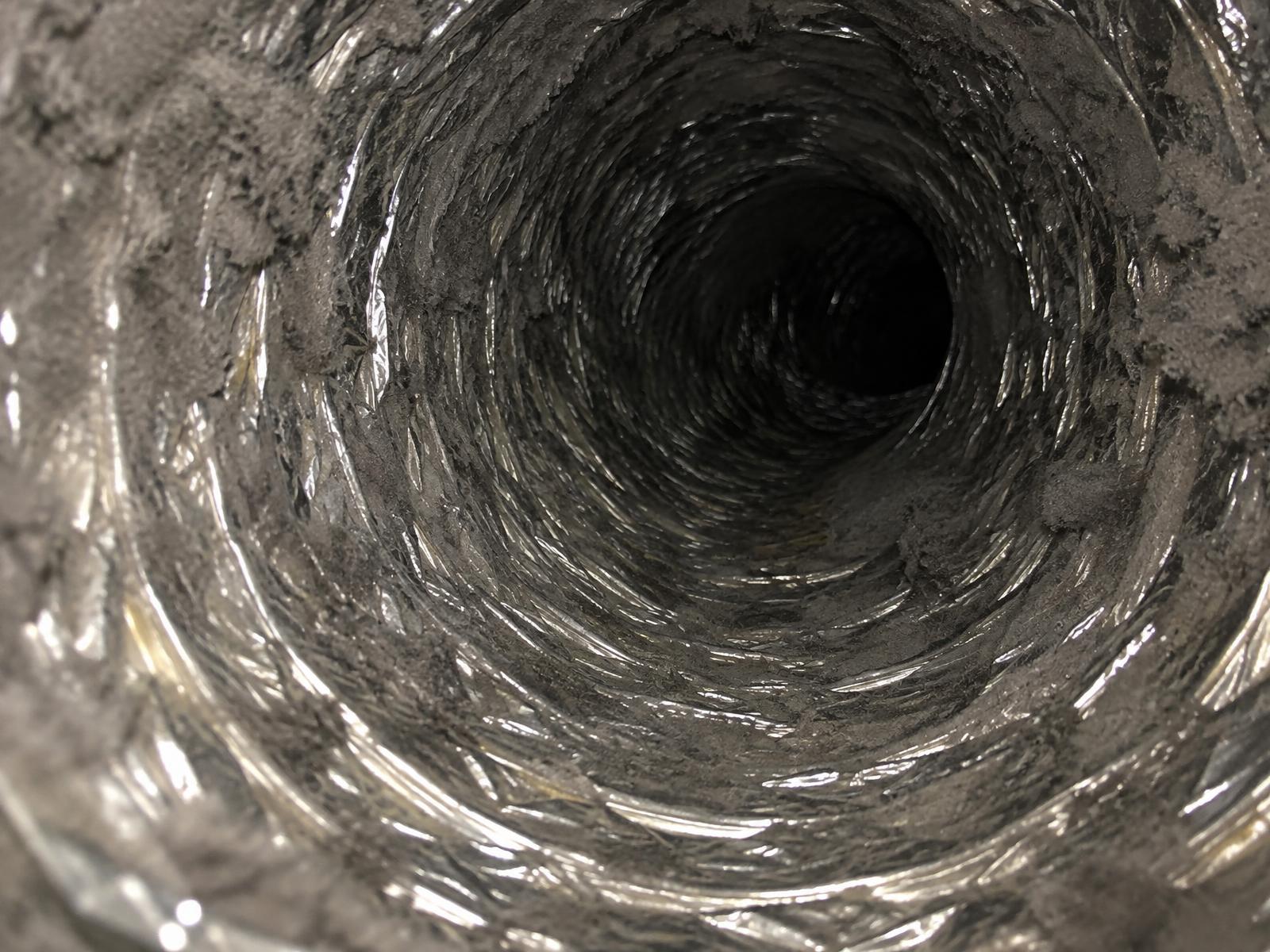 Inside a flexible air duct, the ribbed liner packed with grey dust and lint